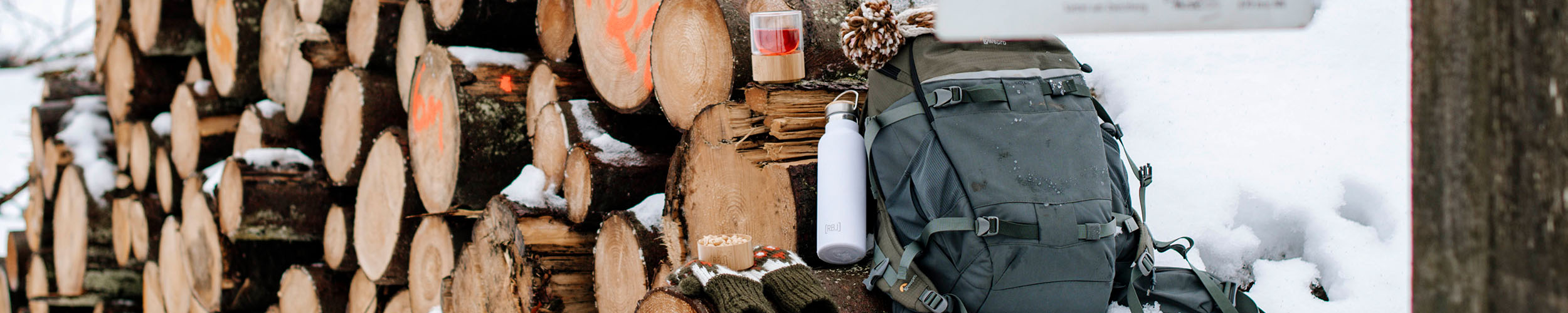 Holzstapel mit Thermosflasche, Rucksack und Teeglas