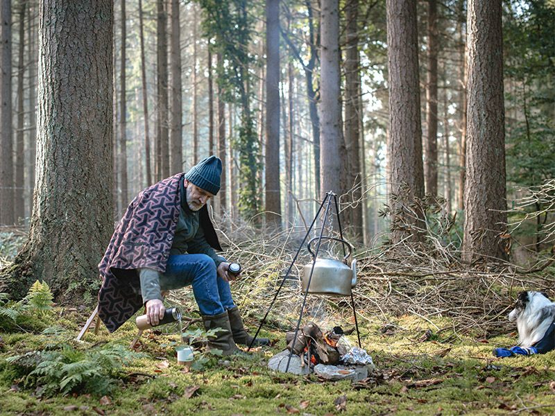 Alter Mann im Wald mit Wärmedecke über den Schultern